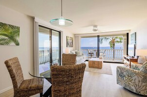 Un vaste salon avec un balcon donnant sur la mer, aménagé avec des fauteuils en osier et un canapé, ainsi qu’un ventilateur de plafond.