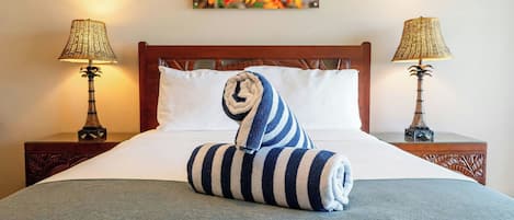 A neatly made bed with a striped towel, two bedside lamps, and a painting on the wall.