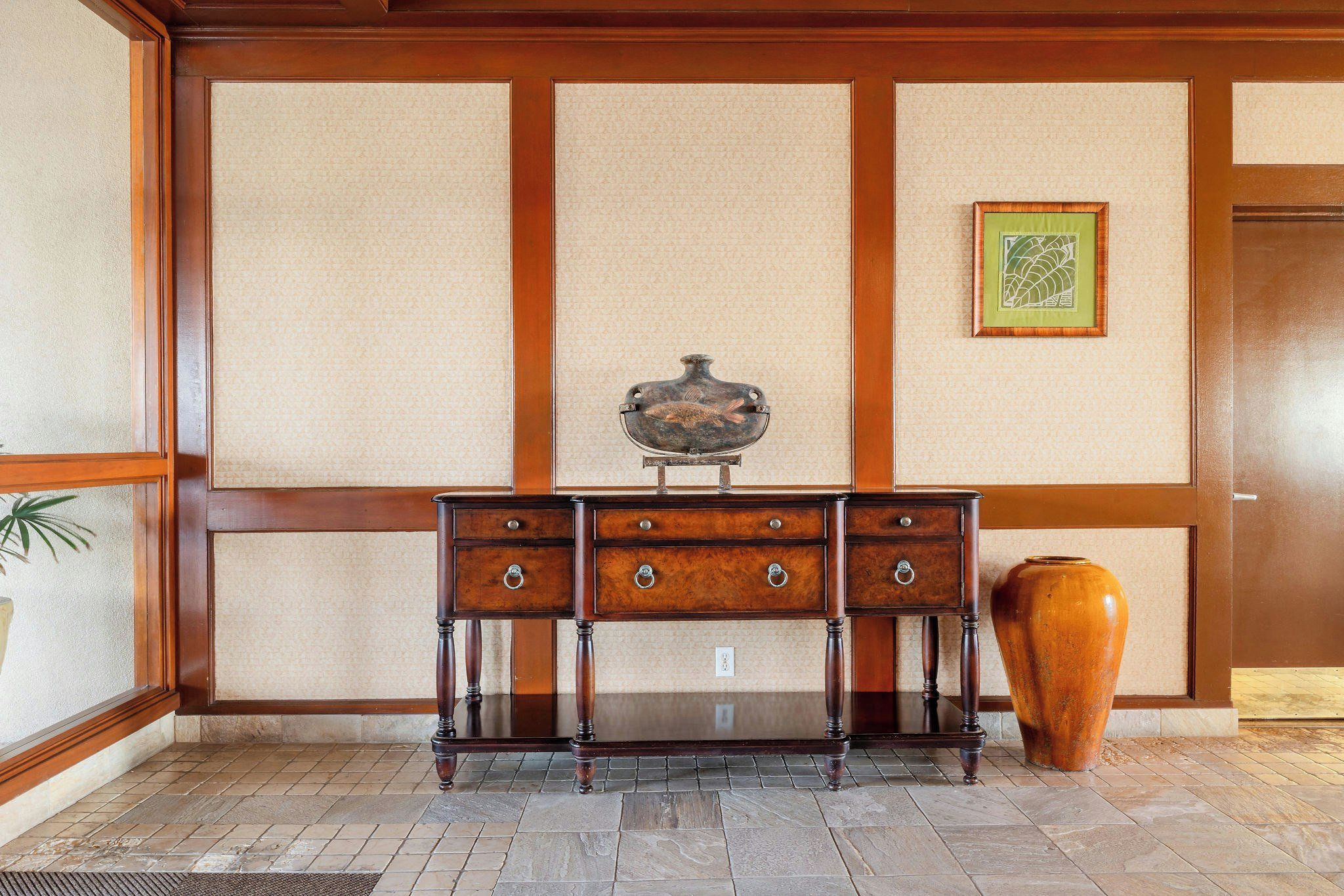 A traditional Japanese-style room with tatami flooring, a dark wooden desk with drawers, a decorative fish-shaped object on the desk, and a large vase on the floor.