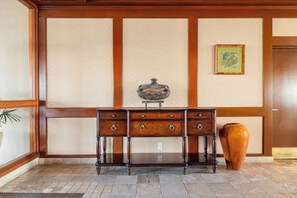 Ein traditioneller japanischer Raum mit Tatami-Bodenbelag, einem dunklen Holztisch mit Schubladen, einem dekorativen, fischförmigen Gegenstand auf dem Tisch und einer großen Vase auf dem Boden.