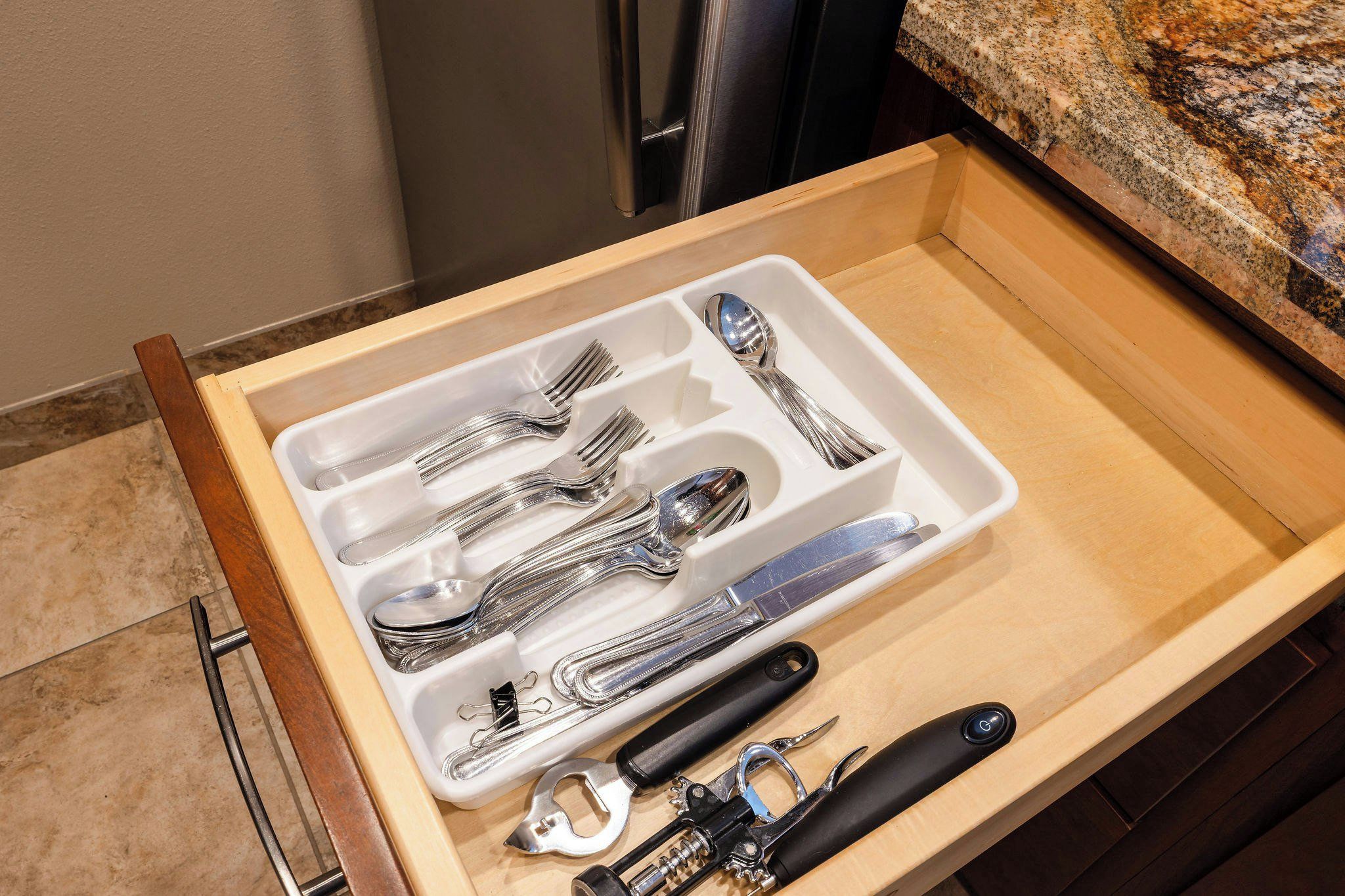 A drawer with kitchen utensils including forks, spoons, a whisk, and a can opener.