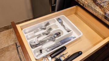 A drawer with kitchen utensils including forks, spoons, a whisk, and a can opener.