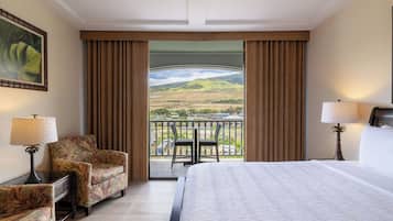 A hotel room with a bed, two chairs, a table, and a balcony with a view of the countryside.