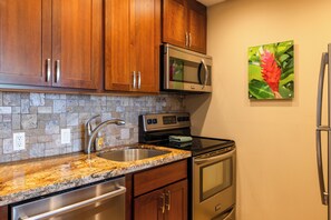 A kitchen with wooden cabinets, a granite countertop, a stainless steel sink, a microwave, an oven, and a refrigerator.