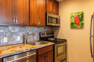 Una cocina con armarios de madera, encimera de granito, pileta de acero inoxidable, microondas, horno y refrigerador.