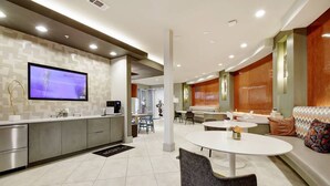 A modern hotel lobby with a kitchen area, a flat-screen TV, and a seating area with a round table. - Luxury Apartment with Fast Wi-Fi  and Free Parking (San Antonio)