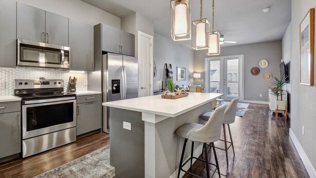 A modern kitchen with stainless steel appliances, a central island with bar stools, pendant lighting, and a view to the dining area. - Luxury Apartment with Fast Wi-Fi  and Free Parking (San Antonio)