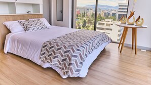 Ein modernes Schlafzimmer mit einem großen Bett, Blick auf die Stadt und einem kleinen Tisch mit Dekoration.