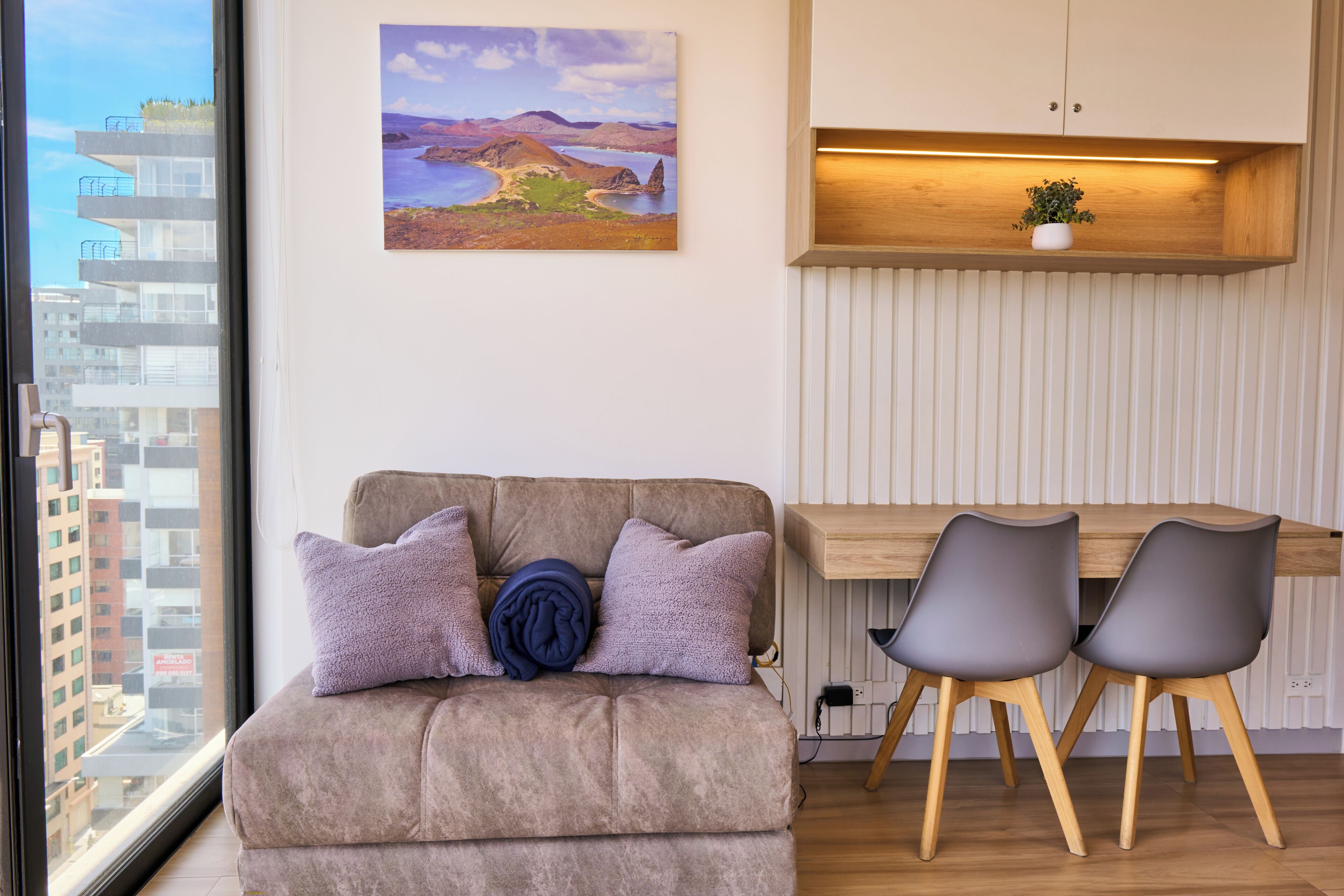 A modern living room with a sofa, two chairs, a wooden desk, a wall-mounted shelf with a plant, and a painting of a landscape.