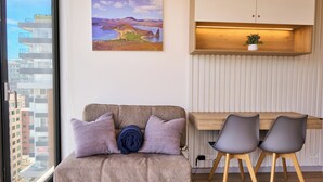 Ein modernes Wohnzimmer mit einer Couch, zwei Sesseln, einem Holztisch, einer Wandablage mit einer Pflanze und einem Landschaftsbild.