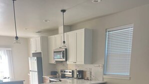 A modern kitchen with white cabinets, a central island with stools, a dining table, and a leather sofa. - Minutes to midtown-New Build Urban Retreat (Sacramento)