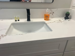 Ein Waschtisch mit Spiegel darüber, einem schwarzen Wasserhahn und zwei Seifenspendern auf der Ablagefläche.