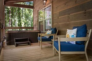 A wooden deck with a bench and a small table, a wooden wall with a window, and a view of trees. - Let It Be Lodge - Pet Friendly | Hot Tub | Fire Pit (Mineral Bluff)