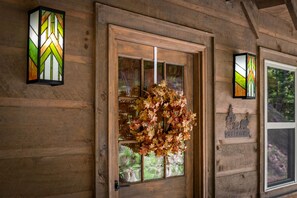 A wooden cabin door with a glass panel, a wreath, and two wall-mounted lights. - Let It Be Lodge - Pet Friendly | Hot Tub | Fire Pit (Mineral Bluff)