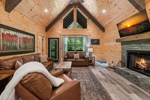 A log cabin interior with a fireplace, leather furniture, and a painting of a forest. - Let It Be Lodge - Pet Friendly | Hot Tub | Fire Pit (Mineral Bluff)