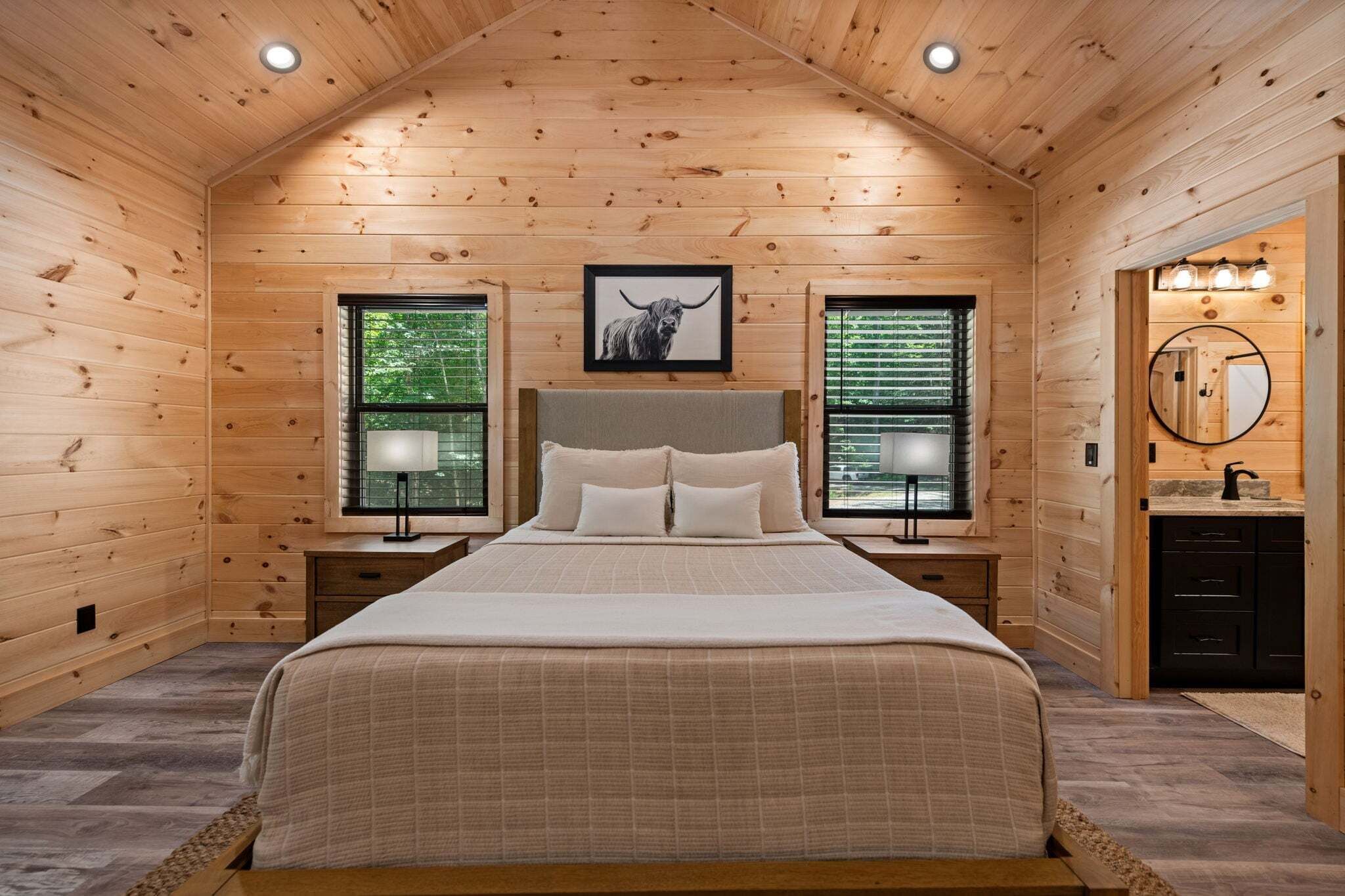 Une chambre à coucher dans une cabane en bois, comprenant un lit, deux tables de chevet, une tête de lit et deux fenêtres équipées de stores.