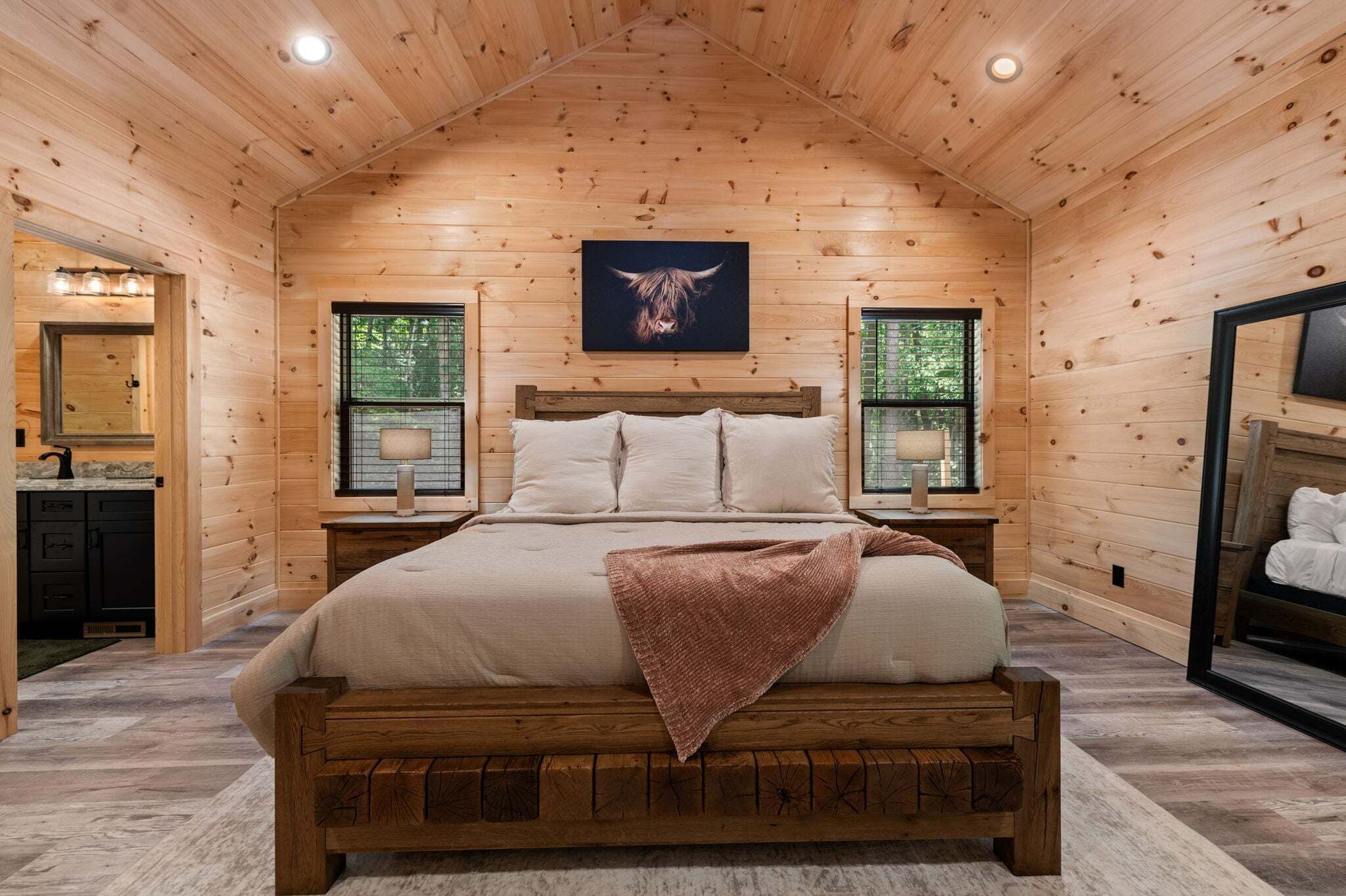 A wooden-paneled bedroom with a bed, two bedside tables, a mirror, and a window.