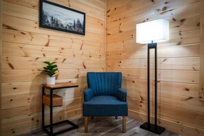 A corner room with wooden walls, a blue armchair, a floor lamp, a small table with a plant, and a framed picture. - Let It Be Lodge - Pet Friendly | Hot Tub | Fire Pit (Mineral Bluff)