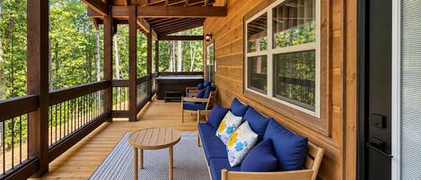 A wooden deck with a sofa and a table, surrounded by windows and a view of trees.