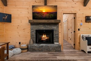 L’intérieur d’une cabane en rondins, avec une cheminée, un tableau représentant un coucher de soleil accroché au mur et une pancarte indiquant : « Restons chez nous ».