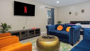Moderni olohuone, jossa on televisio, sininen sohva, oranssi nojatuoli ja pyöreä kultainen pöytä.