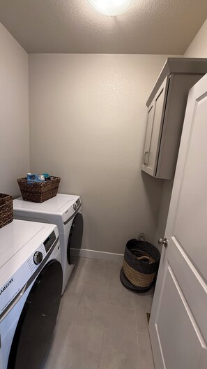 A laundry room with a front-loading washer and dryer, wicker baskets, and a door leading to another room.