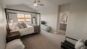 Ein Schlafzimmer mit Bett, Nachttischen, Deckenventilator, Fernseher und Blick auf ein Gewässer.