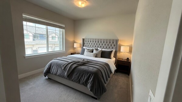 A bedroom with a large bed, two bedside tables, a window, and a ceiling light.