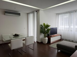 Una sala de estar moderna con una mesa de comedor de vidrio, sillas blancas, un sofá, un televisor y una planta en maceta.