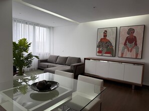 A modern living room with a glass dining table, grey sofa, white cabinet, and two abstract paintings on the wall. - AZORES PICO SALOMÃO T2 - H (Ponta Delgada)