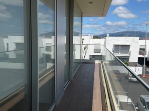 Un balcó amb grans finestres de vidre, vista a edificis moderns i un cel serè.