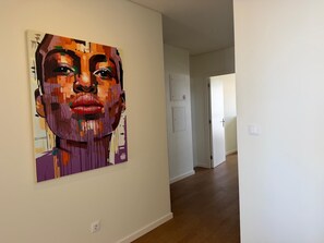 A hallway with a large abstract painting on the wall, a door, and a light switch. - Azores Paim 2-Bedroom Apartment 21 (Ponta Delgada)