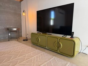 A modern living room with a large flat-screen TV mounted on a green cabinet, a small round table, and a floor lamp. - AZORES OLD ROAD (São Roque)