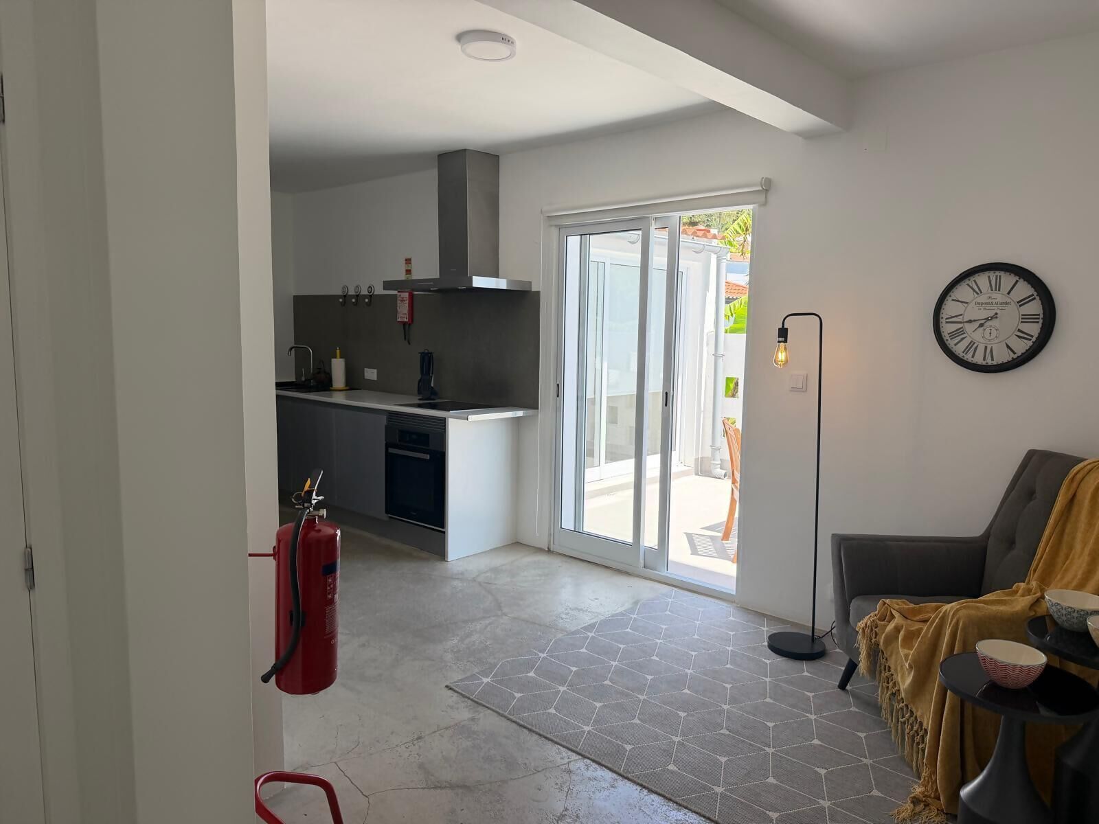 A modern kitchen with a sliding glass door leading to a patio, a dining area with a sofa and table, and a wall-mounted clock.