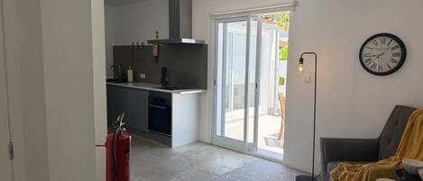 A modern kitchen with a sliding glass door leading to a patio, a dining area with a sofa and table, and a wall-mounted clock.