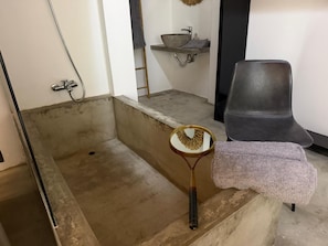 A bathroom with a bathtub, a round mirror, a towel, and a chair. - AZORES OLD ROAD (São Roque)