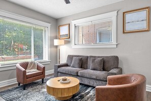 A living room with a grey sofa, two armchairs, a round coffee table, and a lamp. - The Grove | Pet Friendly + Fenced Backyard (Saint Louis)