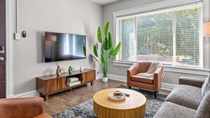 A living room with a flat-screen TV, a large plant, a brown leather chair, a round coffee table, and a sofa. - The Oak | Pet-Friendly King Retreat (Saint Louis)