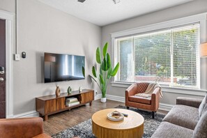 A living room with a flat-screen TV, a large plant, a brown leather chair, a round coffee table, and a sofa. - The Oak | Pet-Friendly King Retreat (Saint Louis)