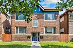 A two-story brick building with a blue front door, windows, and a small front yard. - The Oak | Pet-Friendly King Retreat (Saint Louis)