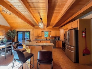 Interior de una cabaña de madera con cocina, comedor y un ventanal grande.