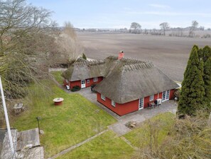 A rural property with two thatched-roof cottages, a grassy yard, and a large open field in the background. - 5 Star Holiday Home in Otterup (Otterup)