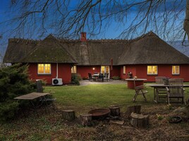 Una cabaña con techo de paja y fachada roja, un patio con mobiliario exterior y un césped bien cuidado.