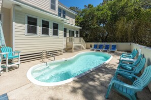 Ein Schwimmbad mit blauen Stühlen, einer Holzterrasse und einem Haus mit weißem Putz.