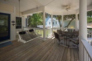 A porch with a swing, a table with chairs, and a view of a house. - Tuck Away: New Rental, Dog-friendly, Private Pool (Corolla)