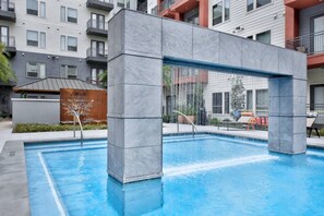 Ein Schwimmbecken mit modernem Design, umgeben von einem mehrstöckigen Gebäude mit Balkonen.