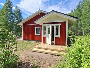 Una casa de madera roja con un porche y una puerta, rodeada de vegetación.