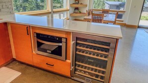 A kitchen with a built-in oven, a wine cooler, and a view of a forest through large windows. - The Lookout | Wifi, AC, Modern (Packwood)