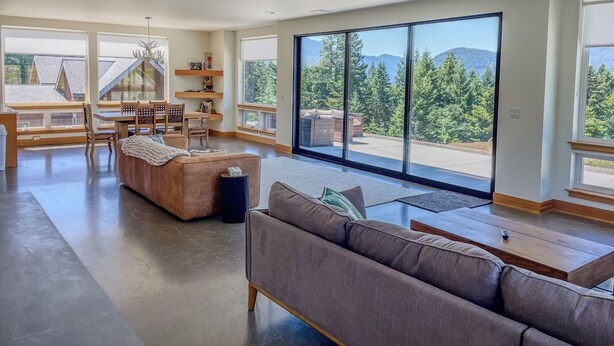A spacious living room with a large sliding glass door leading to a balcony, a wooden dining table, and a cozy seating area. - The Lookout | Wifi, AC, Modern (Packwood)