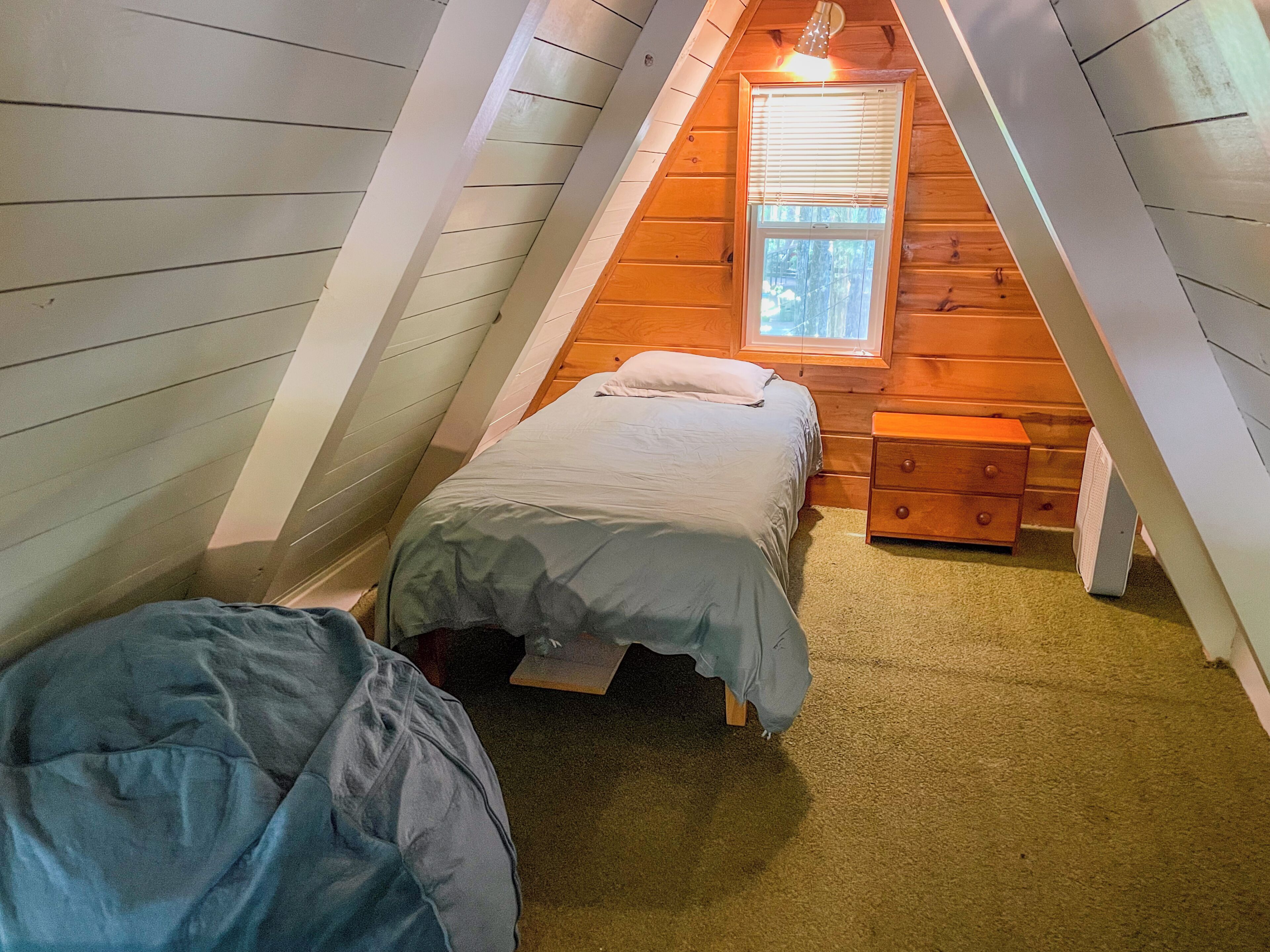 Una piccola e accogliente camera da letto in mansarda, con un letto singolo, un comodino e una finestra.